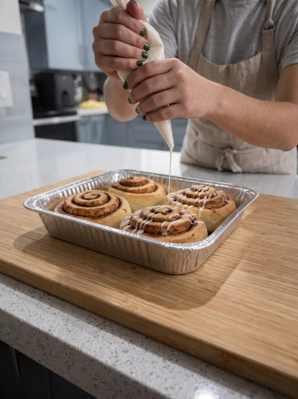 The baker drizzling icing over four cinnamon rolls in a baking tray.