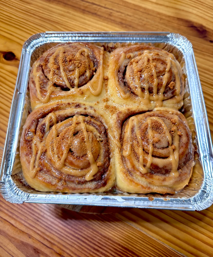 Four cinnamon rolls with a light caramel Biscoff glaze and cookie crumble in a tray