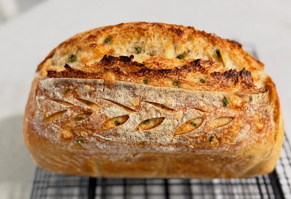 A sourdough boule with subtle cheddar and jalapeño flecks on a cooling rack