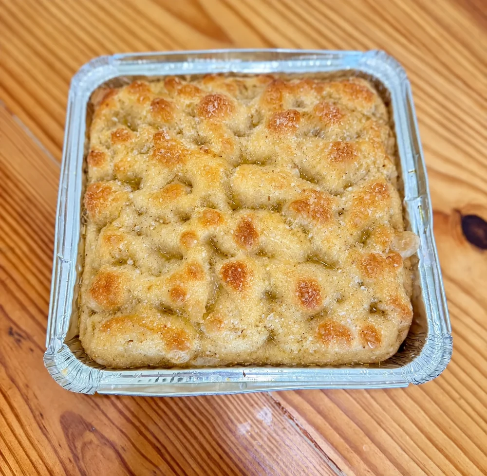 Plain sourdough focaccia with a golden olive-oil top in a tray